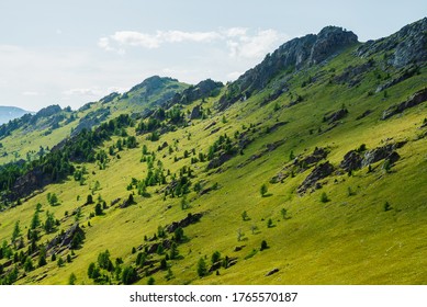 Green mountain scenery with vivid green mountainside with conifer forest and big crags under clear blue sky. Coniferous trees and big rocks on hillside. Scenic landscape with big stones on steep slope - Shutterstock ID 1765570187