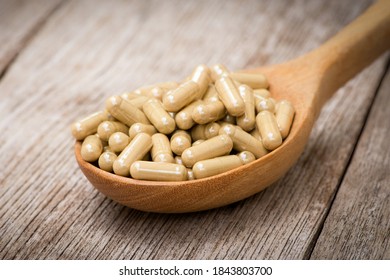 Green natural herbal medicine capsules pill in wooden spoon isolated on wood table background. Alternative supplement concept. Vintage dark tone.