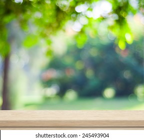 Green Nature Background, Empty Wooden Deck Table Over Blur Tree Garden Park With Bokeh In Spring Summer Outdoor Background, Wood Shelf, Counter, Desk Surface For Food Picnic, Product Display Montage