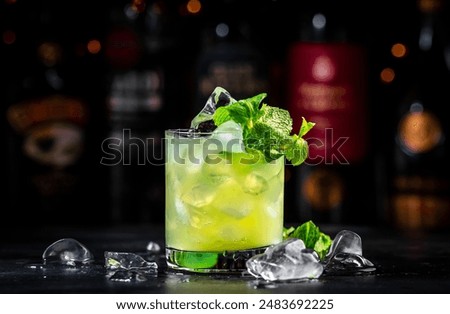 Green Negroni cocktail drink with gin, aperitif, liqueur, mint and ice. Black bar counter background with bottles 