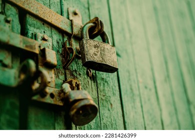  The green old wooden gate is closed with a rusty latch and a metal padlock. Vintage. Old architectural details.