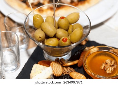 Green olives in a glass bowl served with cheese, crackers, nuts, and honey on a rustic table, concept of Mediterranean appetizer platter