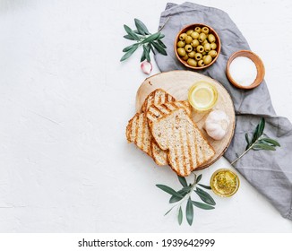 Green olives with olive oil with fresh baked ciabatta bread,  salt and young olive branches over white background. Flat lay, space - Powered by Shutterstock