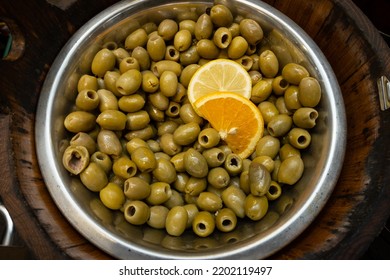 Green Olives On Display In A Silver Bowl On A Stall In A Market Place Where Fresh Food Is Bought By People Who Like Healthy Mediterranean Food. The Tasty Nibble Is Garnished With Range And Lemon