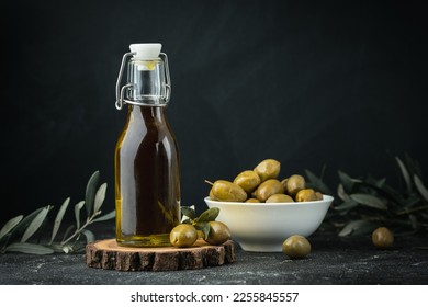 Green olives in a white bowl next to a bottle with olive oil and leaves on a black background. Bottle of cold pressed oil. Traditional Greek and Italian food. - Powered by Shutterstock
