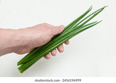 Green onion in hand against white table background, natural cooking ingredients, green fresh onions, close-up - Powered by Shutterstock