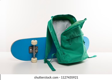 Green Open Backpack Next To A Blue Skateboard, Back To School. Empty School Bag