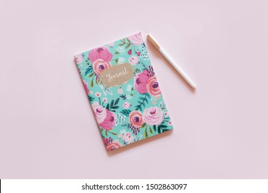 Green, Orange, Tan Notebook With Rose Gold Phone And White Pen On A Pink Background