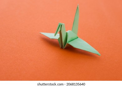 Green Origami Paper Crane On Orange Background.