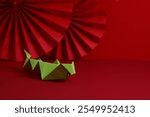 Green origami snake on a vibrant red background with an abstract paper fans pattern. Happy Chinese New Year, Year of the snake concept.