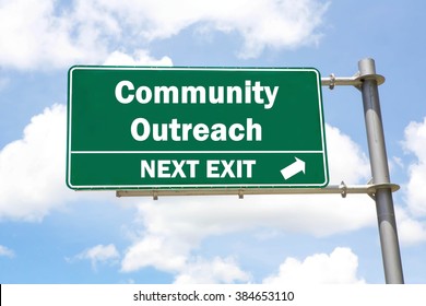 Green Overhead Road Sign With A Community Outreach Next Exit Concept Against A Partly Cloudy Sky Background.