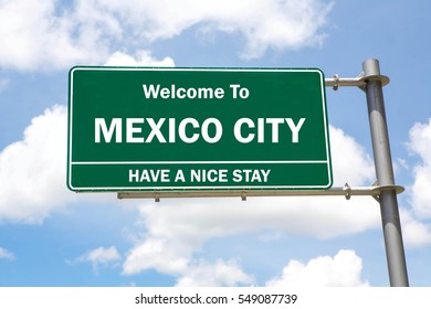 Green Overhead Road Sign With A Welcome To Mexico City, Have A Nice Stay Concept Against A Partly Cloudy Sky Background.