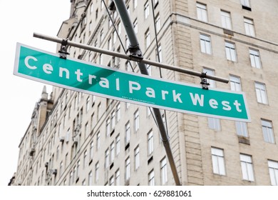 Green Overhead Street Sign Depicting It Is Central Park West In Manhattan, New-York, With A High Rise Residential Building In The Background.