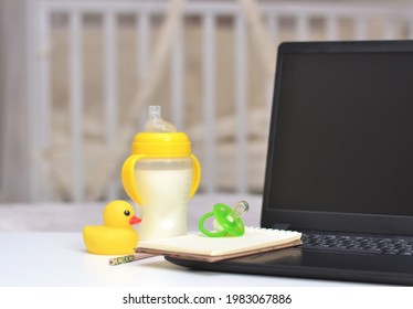 green Pacifier, notebook on the laptop, yellow baby bottle and duck toy cot background. 
Working in a decree. Maternity leave concept.  - Shutterstock ID 1983067886