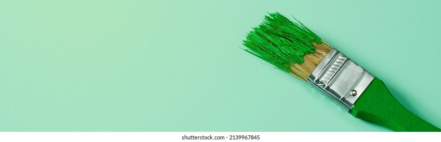 a green paintbrush with some green paint, on a pale green background with some blank space on the left, in a panoramic format to use as web banner or header