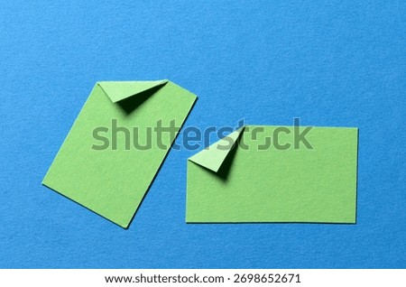 Green paper message notes or sheets with folded edge dog-ear earmark and copy space for text on blue background, top view flat lay conceptual desk backdrop