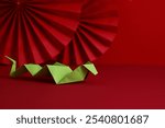 Green paper origami snake with oriental asian style paper fans on red background. Happy Chinese New Year 2025, year of the snake concept. 