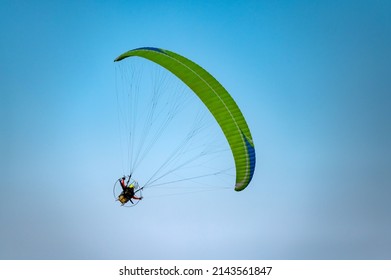 GREEN Paramotor Flying through sunlight with Blue Sky.Adventure man active extreme sport pilot flying in sky with paramotor engine glider parachute.