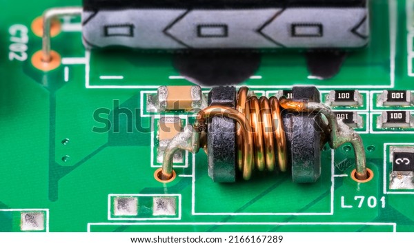 Green PCB detail with electromagnetic\
coil and electronic surface-mount components. Close-up of small\
inductor with copper wire on ferrite core, electrolytic capacitor\
and resistors.\
Electrotechnics.
