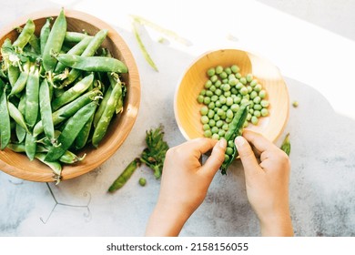 Green pea pods. female hands hold a pod of peas and cleans its wooden bowl on a white background. harvesting concept. healthy vegetables.