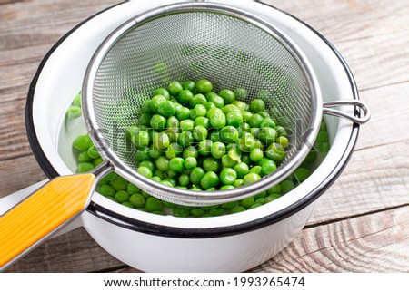 Green peas in a colander. Boiled or blanched vegetables on a wooden table