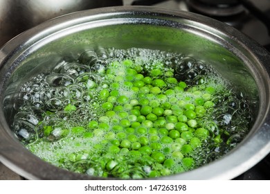 Green peas thawed and cooking in the boiling water in the metal pot on the stove