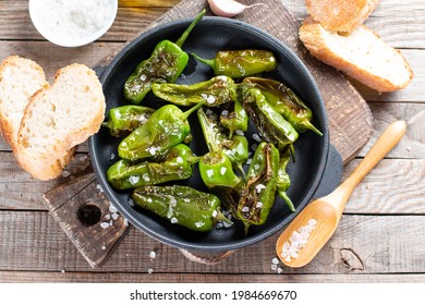 Green pepper Padron baked or fried in the Spanish style in a frying pan on a wooden table. Top view