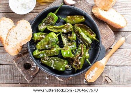 Green pepper Padron baked or fried in the Spanish style in a frying pan on a wooden table. Top view