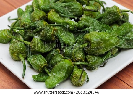 Green pepper Padron baked or fried in the Spanish style on a white plate and wooden background