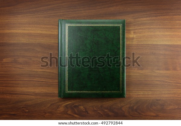 Green Photo album or Year book cover,\
blank, placed on a dark colored wooden\
table.