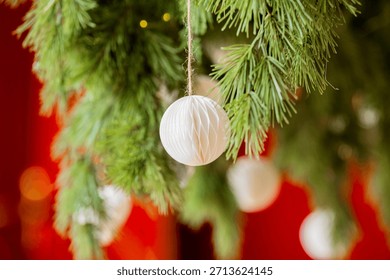 Green pine tree branches with white paper ball ornaments and warm blurred bokeh lights