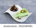 Green pistachio cake with macadamia nuts on white plate on gray concrete table. Creamy pistachio cheesecake