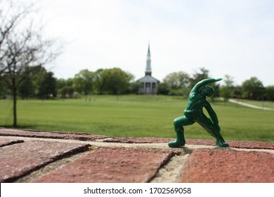 Green Plastic Army Man Figurine Doing Yoga In Front Of A Church