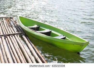 green plastic boat parked at bamboo raft on blue water surface. this image for travel,nature and vehicle concept