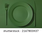 Green plate with colored cutlery on the green background.