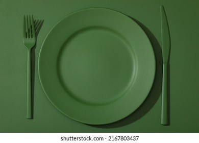 Green plate with colored cutlery on the green background.