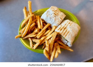 A green plate with French fries and a grilled wrap sandwich cut in half, revealing its filling. The wrap contains vegetables and chicken. - Powered by Shutterstock