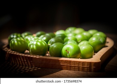 Green plums in a wooden plate.
