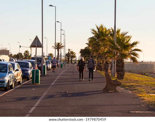 Green Point, Cape Town, South Africa -\
17-05-2021\
\
Sun setting over Green Point. People walking by,\
traffic lights and blue sky in\
background.