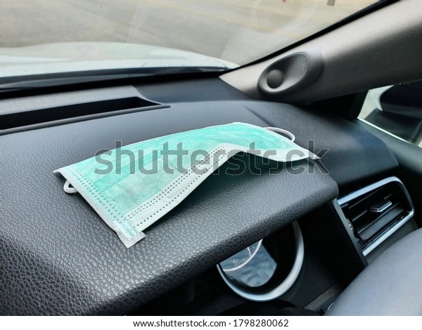 A green protective\
mask to prevent dust or COVID-19 virus placed on the dashboard of\
the car inside the car. Masks are a necessity today because of the\
spread of germs.
