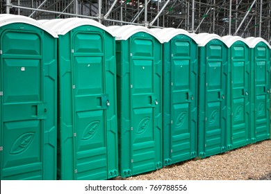 Green public portable toilets with white roofs stand in a row on a city street 