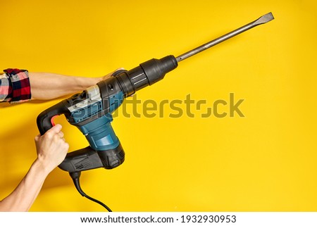 Green Puncher in hands of builder isolated on yellow background. male hand hold new Puncher or drill. Banner with copy space