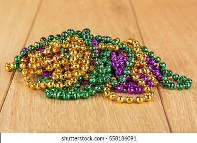 Green, Purple, And Gold Mardi Gras Beads Isolated On Wood