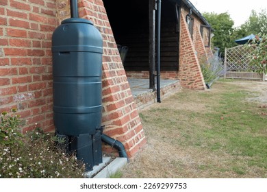 green rainwater tank or water butt connected to a rain collector at the side of a converted barn