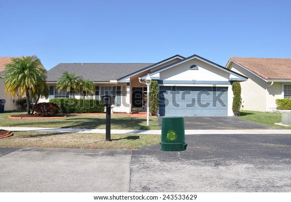 Green Recycle trash\
container Suburban back split style home residential neighborhood\
clear blue sky USA
