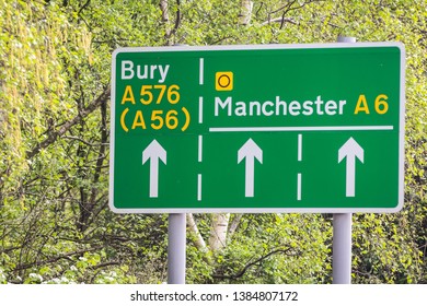 Green Road Signs On A Leafy Background Showing Directions To Manchester And Bury Including The A6 A576 And A56. 
