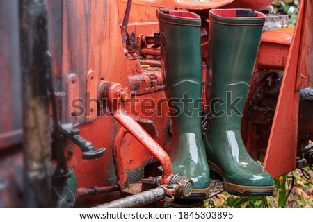 Green rubber boots stand on the step of a bright red tractor in the rain. Wellington boots offer optimal protection on rainy days and are one hundred percent waterproof.