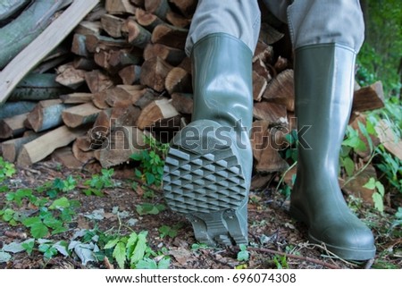 Green rubber boots and a wooden pile in the forest.
