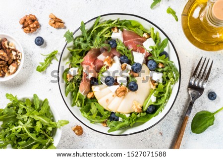 Green salad with arugula, spinach, pear, jamon, blueberries and feta cheese.Top view on white background. Healthy food, low calories dish.