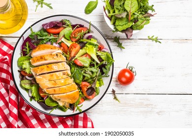 Green salad with baked chicken breast at white kitchen table. Healthy food, clean eating concept. Top view image.